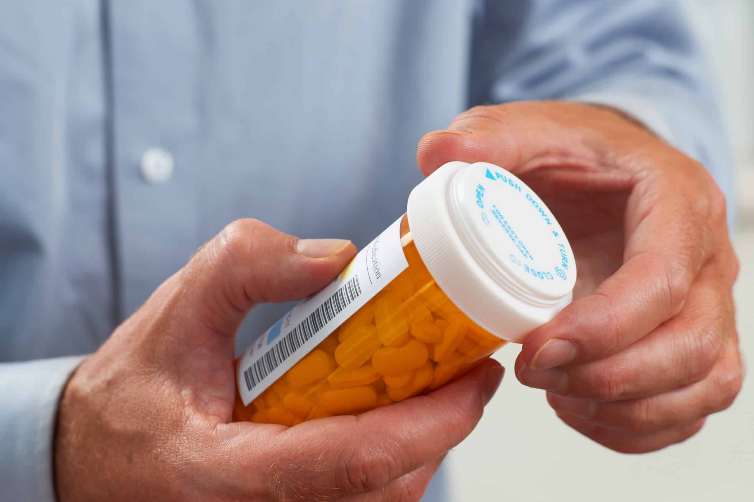 Two older hands clutching and opening a prescription drug bottle