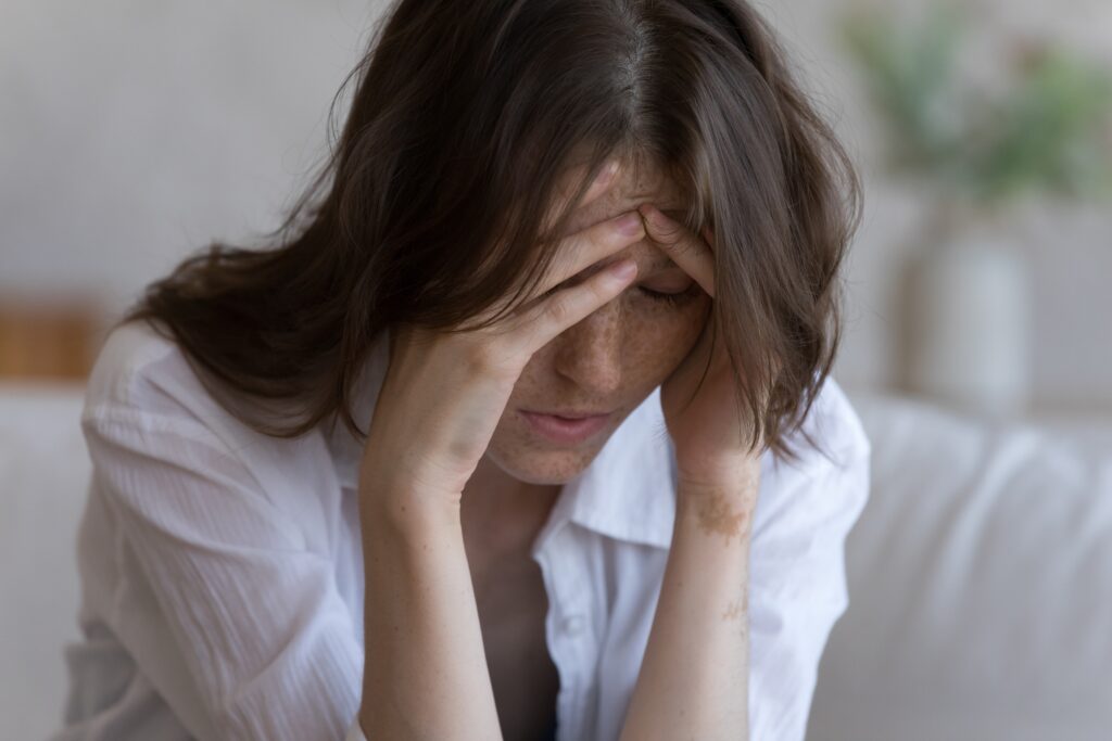 A young woman is bent over with her hands on her temples and forehead has trauma and addiction.