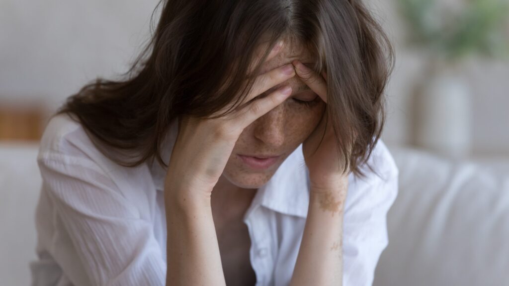 A young woman is bent over with her hands on her temples and forehead has trauma and addiction.