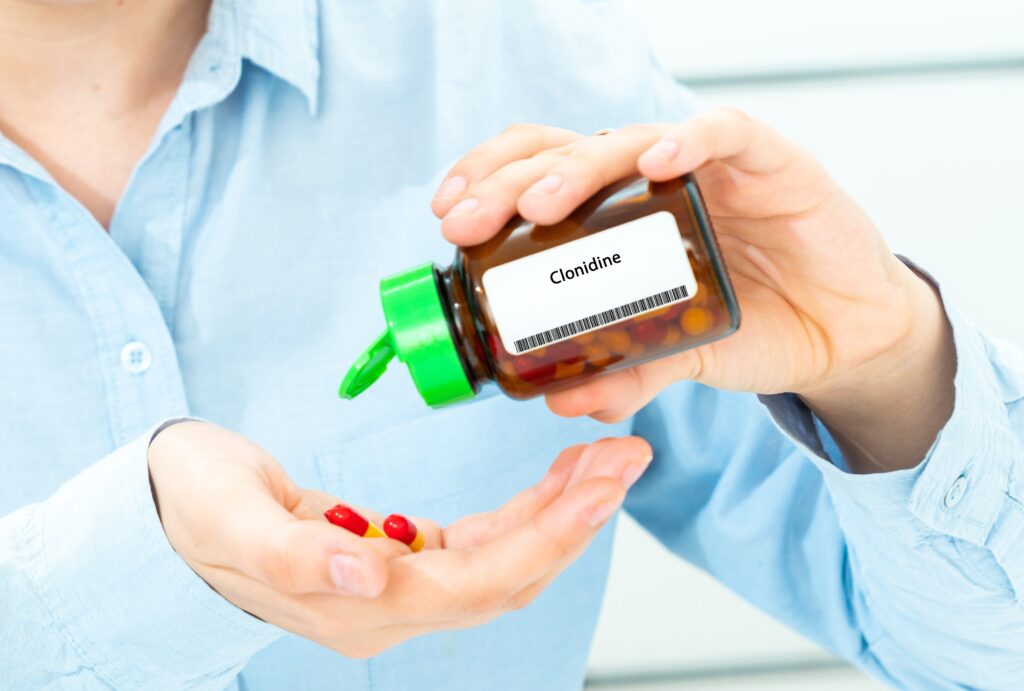 A person in a blue shirt who has clonidine withdrawal is pouring out pills onto their hand from a bottle of clonidine.