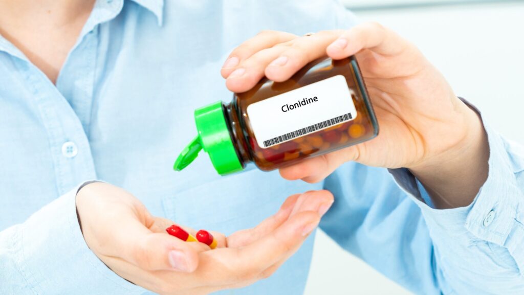 A person in a blue shirt who has clonidine withdrawal is pouring out pills onto their hand from a bottle of clonidine.