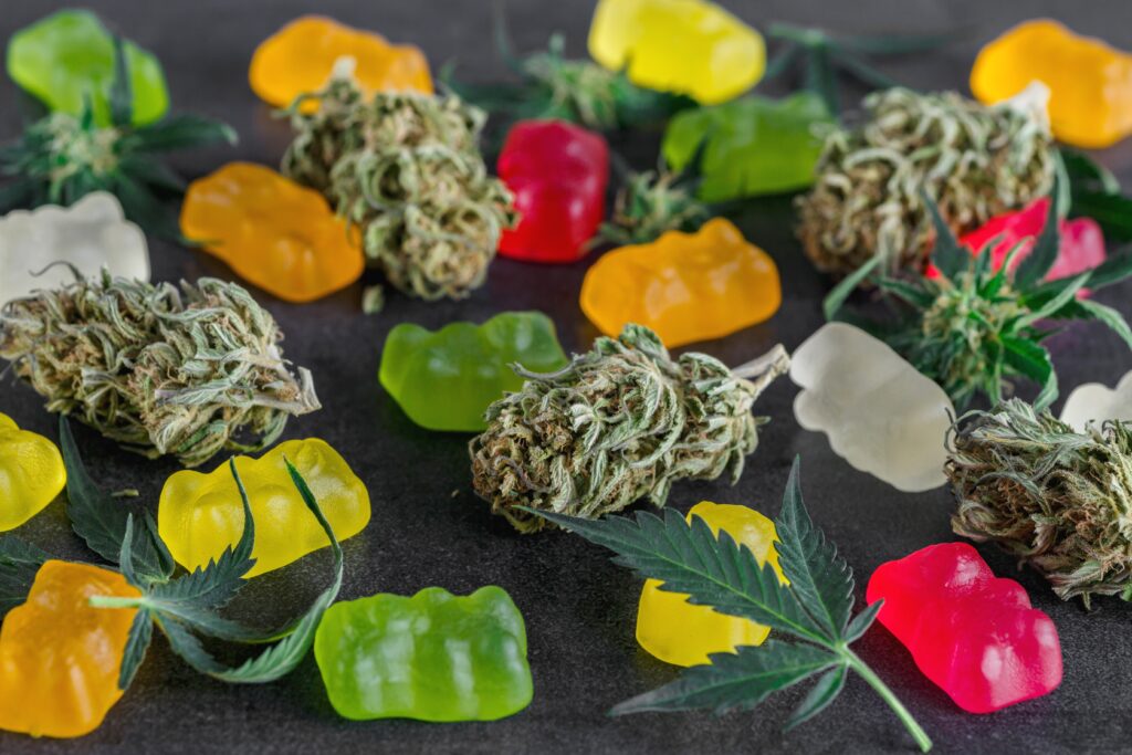 Green, orange, yellow and red cannabis gummies are laid out next to marijuana buds.