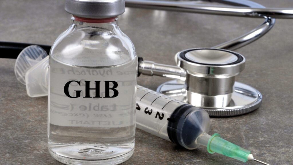 A glass vial of GHB sits next to a syringe and stethoscope represents the side effects you can experience with withdrawal from GHB.