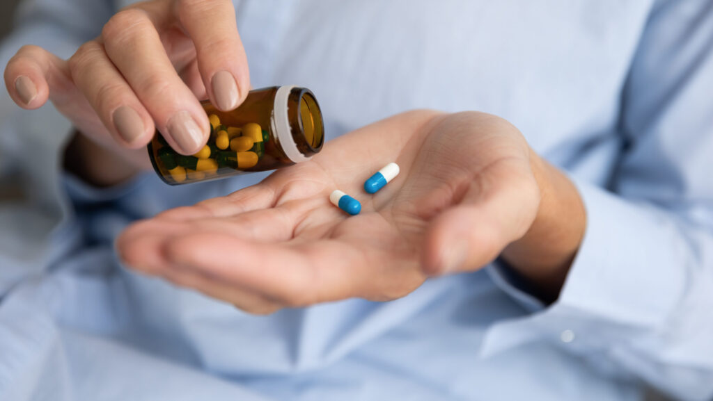 A person is pouring out blue and white pills that represent the arthritis medication meloxicam.