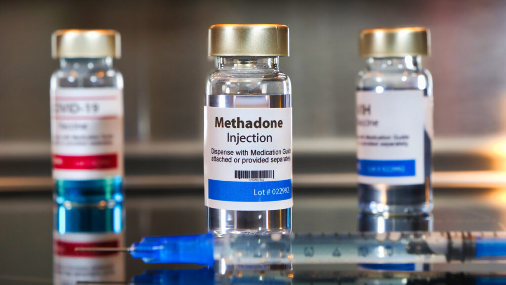 Three glass bottles of liquid methadone sit behind a syringe on a glass table at a methadone clinic.