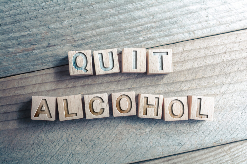 On a wooden table, block tiles spell out the words quite alcohol and reference how to quit alcohol cold turkey.