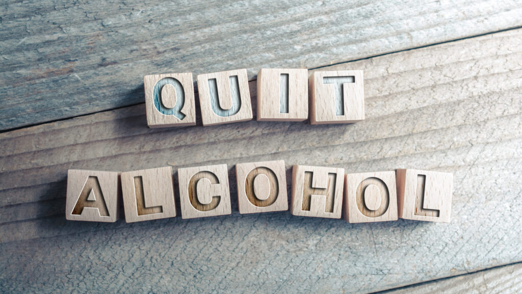 On a wooden table, block tiles spell out the words quite alcohol and reference how to quit alcohol cold turkey.