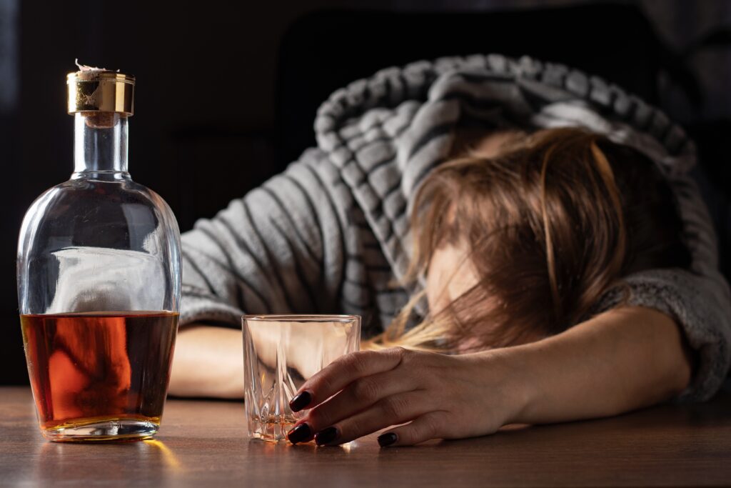 A woman slumped over the table holding a glass of alcohol represents the fact that an alcoholic can probably never drink again after being sober.