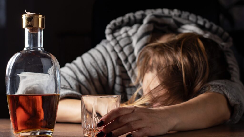 A woman slumped over the table holding a glass of alcohol represents the fact that an alcoholic can probably never drink again after being sober.