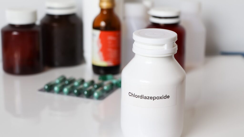 A white table with various bottles and jars of medication including chloridiazepoxide or Librium labeled on a white bottle.