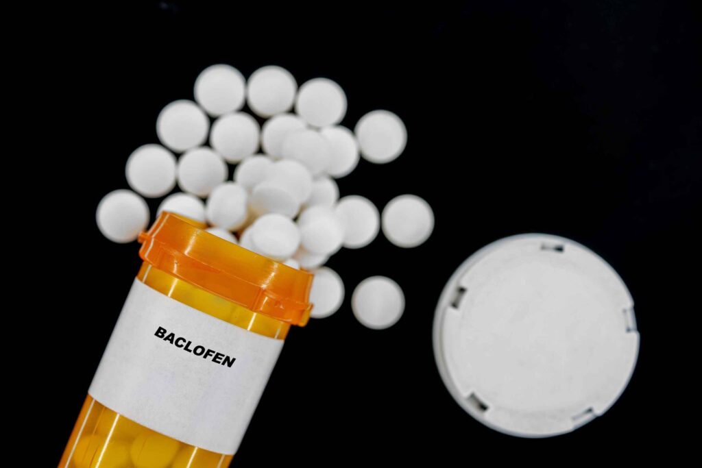 A spilled over pill bottle of white tablets of Baclofen represents the effects of mixing Baclofen and alcohol.