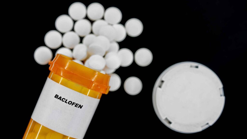 A spilled over pill bottle of white tablets of Baclofen represents the effects of mixing Baclofen and alcohol.