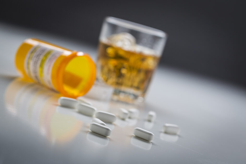 A glass of alcohol next to a tipped over bottle with suboxone pills spilled out representing the dangers of mixing suboxone and alcohol.