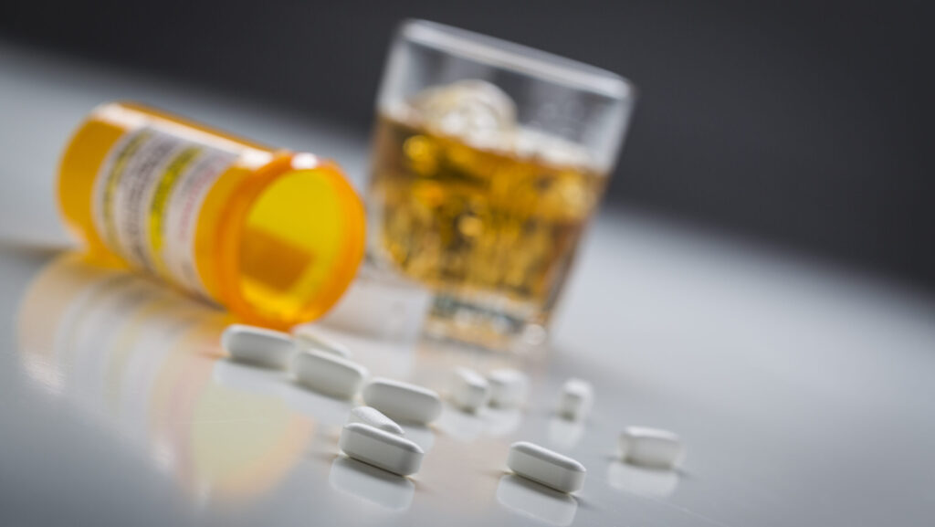 A glass of alcohol next to a tipped over bottle with suboxone pills spilled out representing the dangers of mixing suboxone and alcohol.