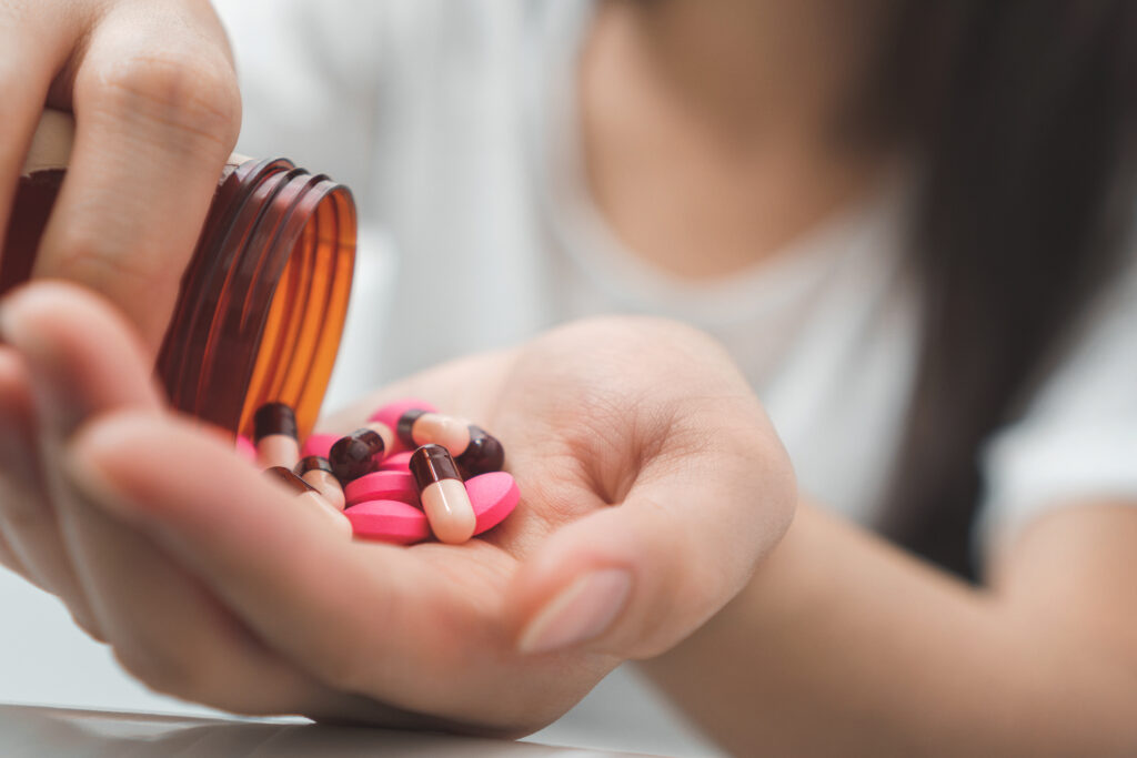 A young woman pours out a bottle of colorful pink Xanax pills and tablets representing an overdose on Xanax.