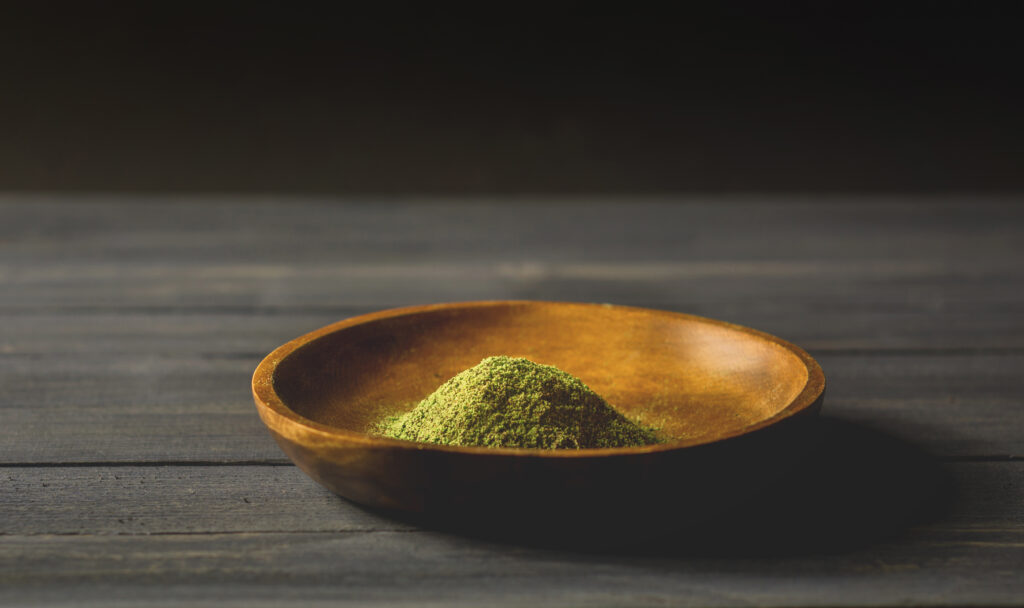 Green kratom powder in a small wooden bowl ready for users as they attempt to snort kratom.