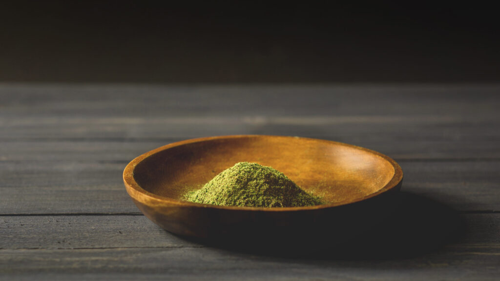 Green kratom powder in a small wooden bowl ready for users as they attempt to snort kratom.