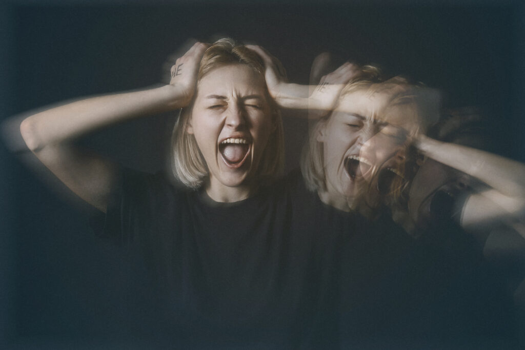 A young woman with short blond hair is screaming and holding her head represents her experiencing meth psychosis.