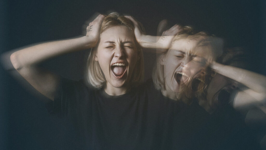 A young woman with short blond hair is screaming and holding her head represents her experiencing meth psychosis.