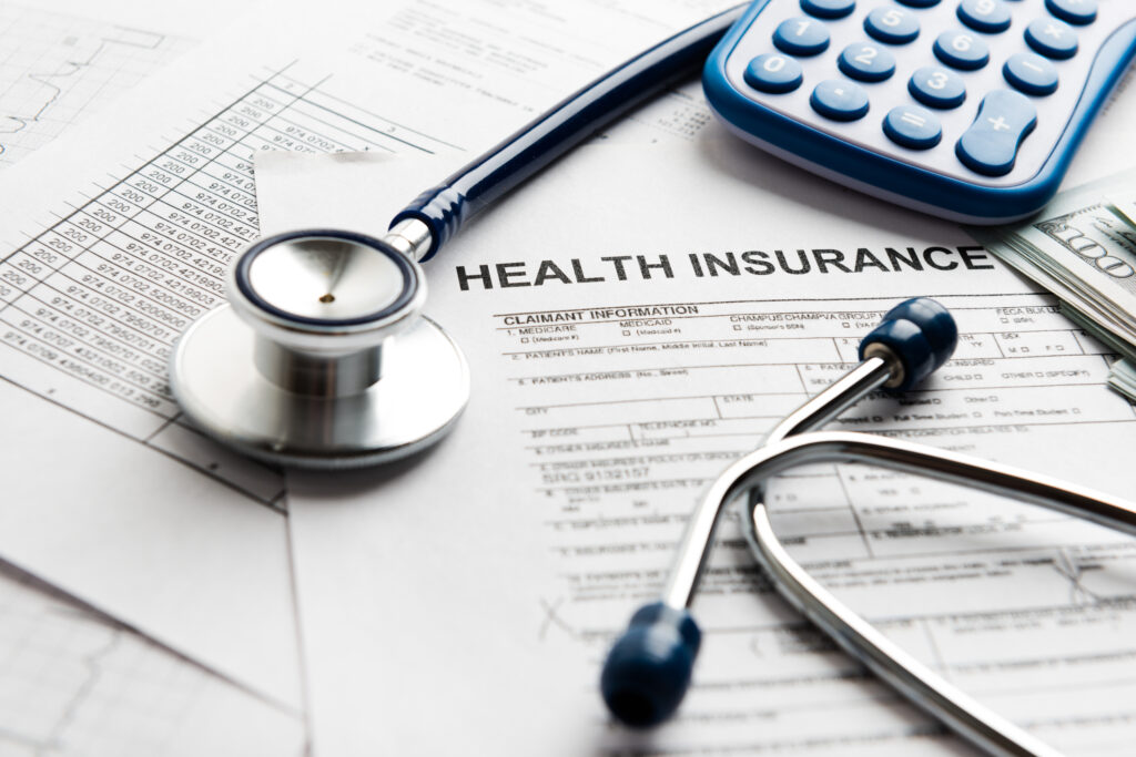 Medical insurance papers lay on a desk with a stethoscope, money and calculator.