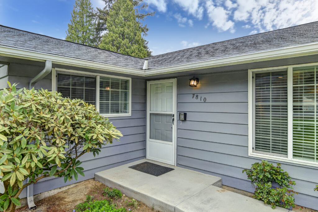 Front of Optum addiction treatment house, gray siding with green plants and white front door