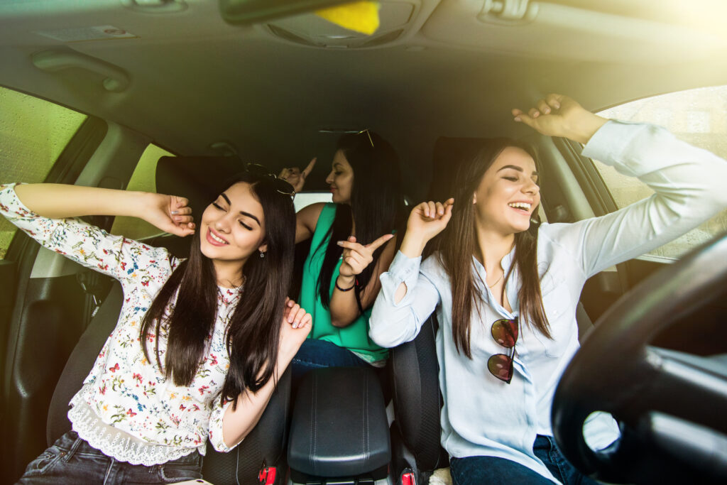 A group of three, young, female sober friends dancing in the car as they embrace their life without drugs.