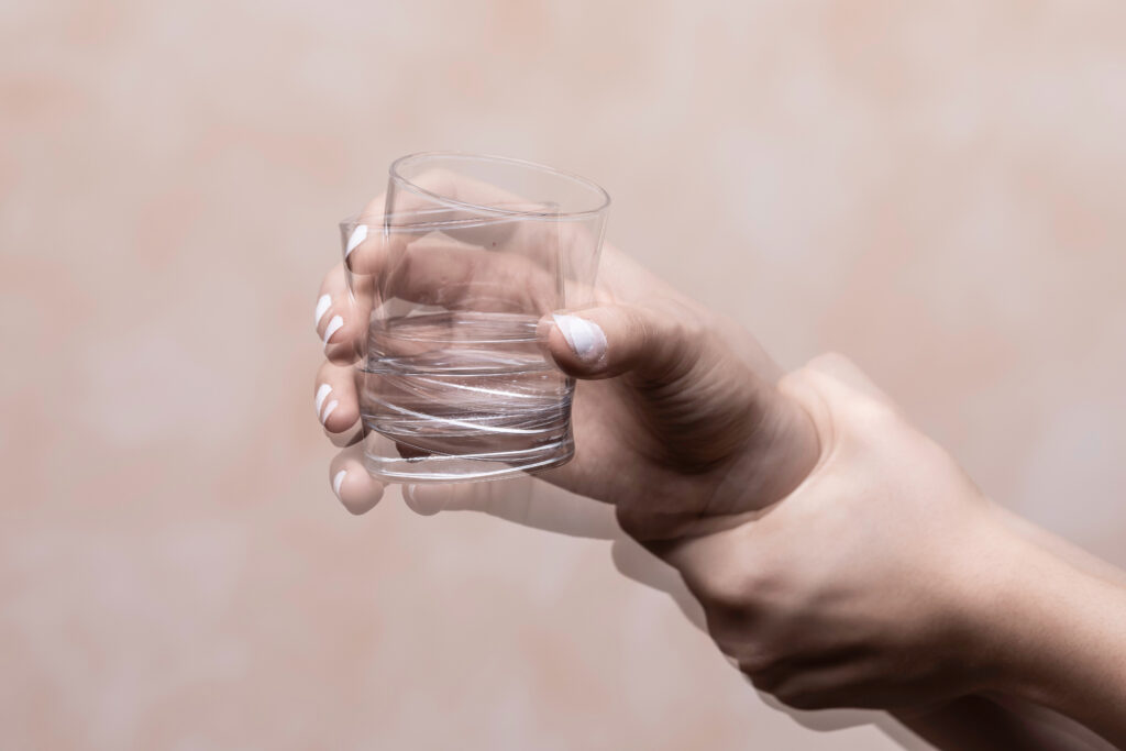 A young woman holding up a glass cup, who cannot stop shaking after drinking alcohol.