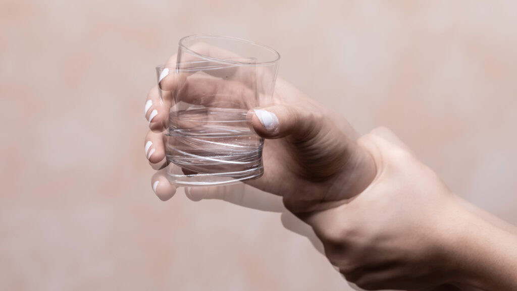 A young woman holding up a glass cup, who cannot stop shaking after drinking alcohol.