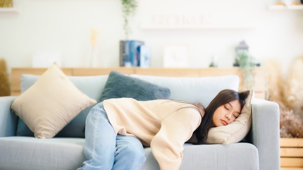 A young women is slouched over to the side of a sofa because she is experiencing a condition called sobriety fatigue.