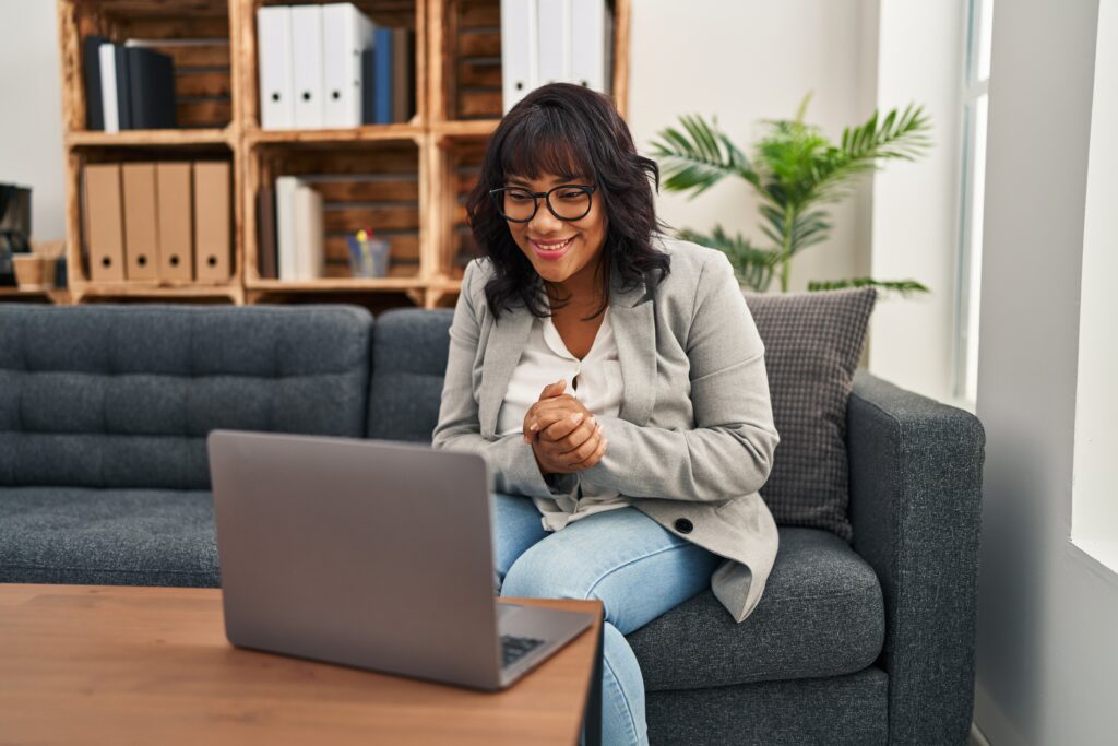 A young women with glasses sitting on the sofa on her laptop engaging in online rehab therapy in the comforts of her home.