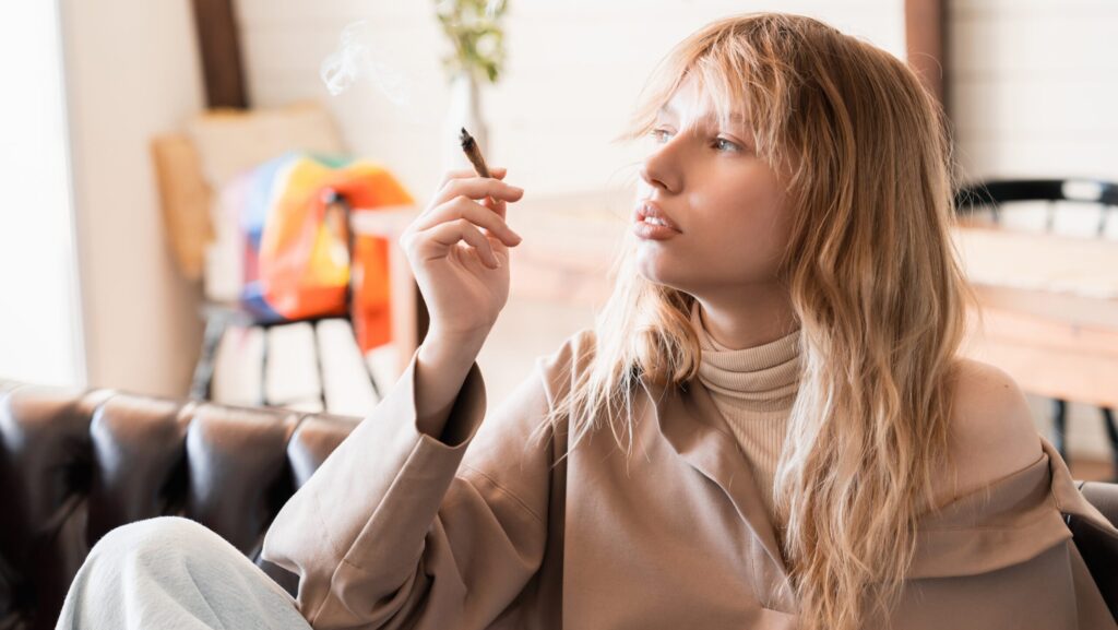 A young woman sitting on a sofa smoking a marijuana blunt participates in the California Sober lifestyle.