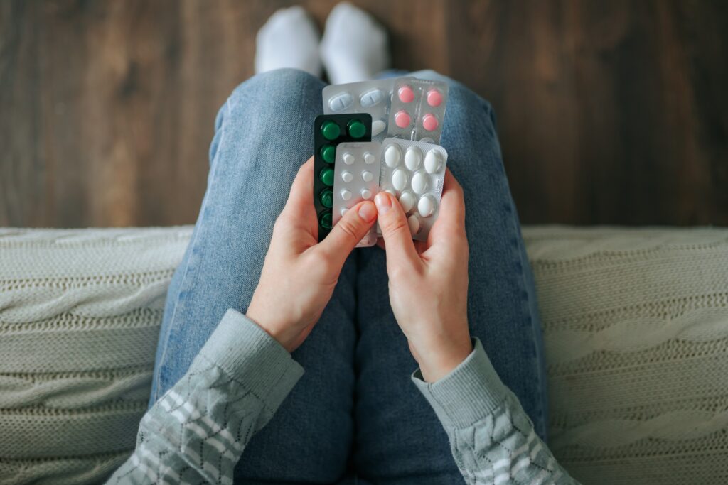 A young person sitting on the edge of their bed holding various pill packets of Klonopin and other drugs.