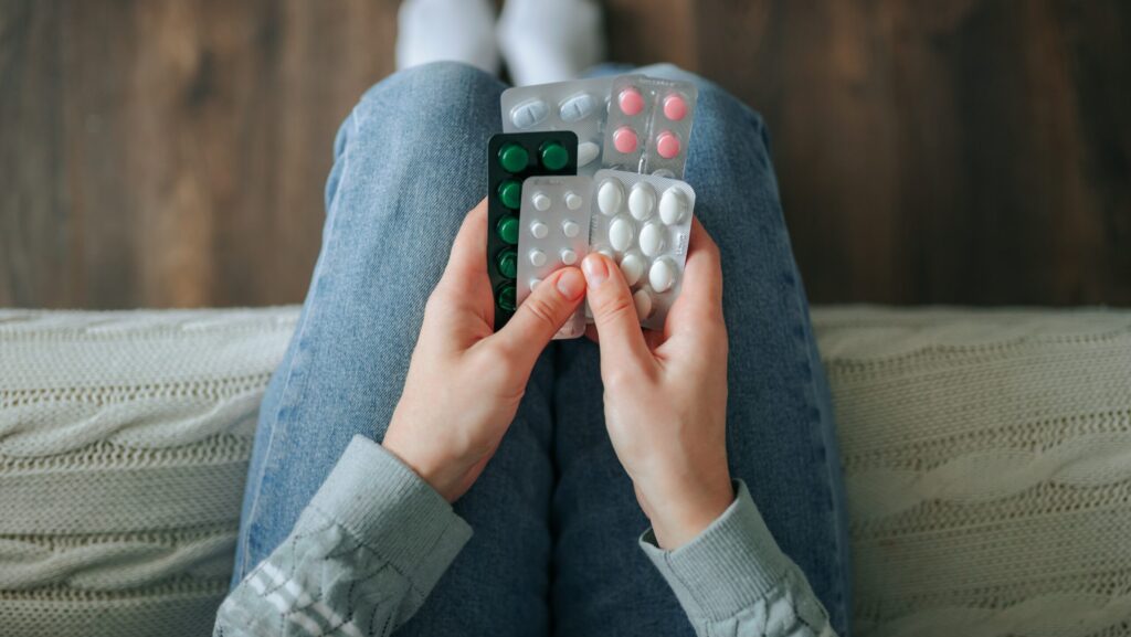 A young person sitting on the edge of their bed holding various pill packets of Klonopin and other drugs.