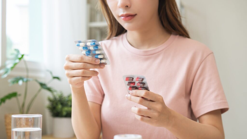 A young women is sitting at a table holding up two different packs of tablets that have resulted in experiencing a paradoxical effect.