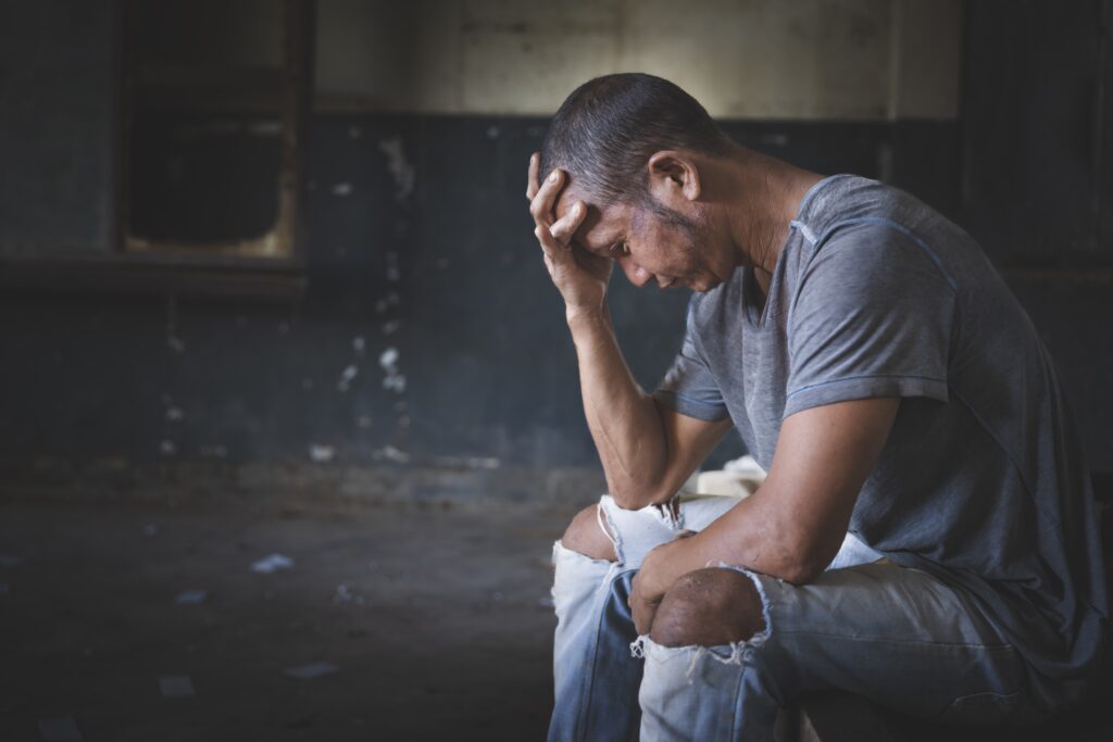 A man in grey shirt and ripped jeans going through withdrawal symptoms you can die from is sitting uncomfortably with his hand covering his face.