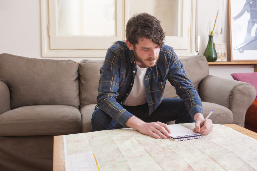 A young man at a sober living home is sitting on the sofa writing on a notepad with pen.