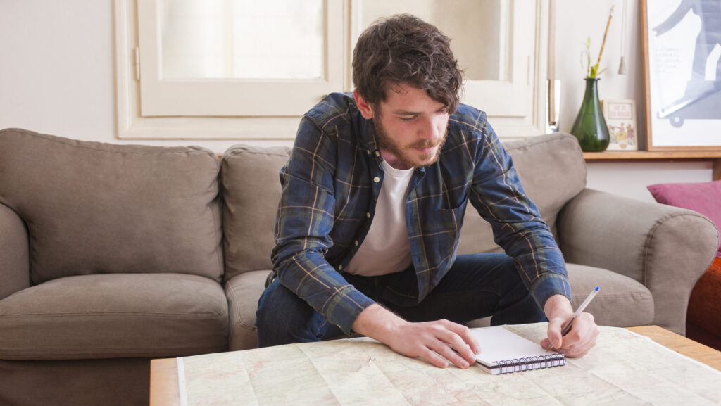 A young man at a sober living home is sitting on the sofa writing on a notepad with pen.