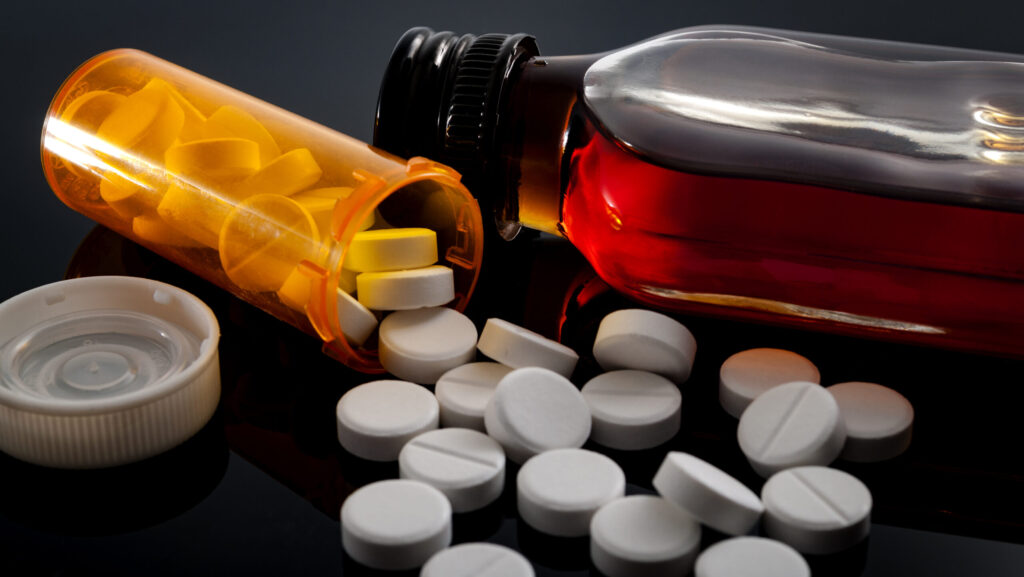 An orange bottle of opioid pills spills over next to a closed bottle of an amber liquid substance represents k18 pills.