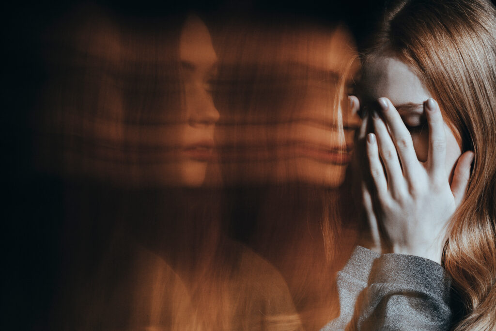 A young women covering her face with her hands experiencing the effects of Adderall and psychosis.