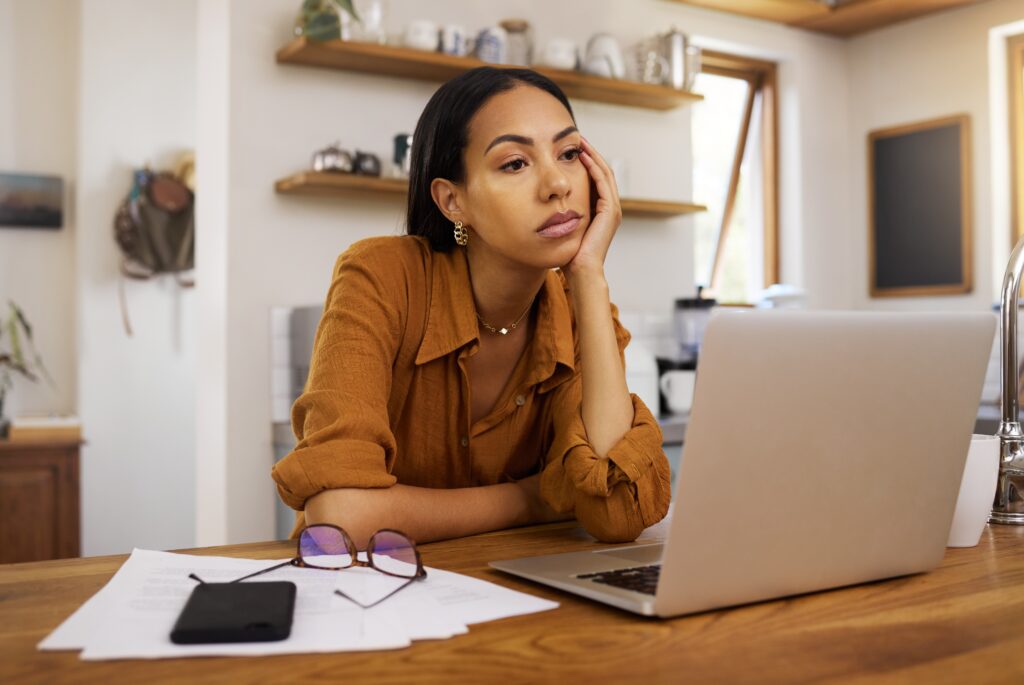 A young woman with alcohol addiction and brain fog sitting mindlessly at her desk in front of her laptop.