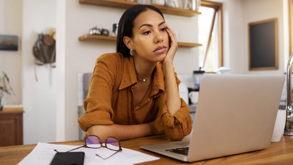 A young woman with alcohol addiction and brain fog sitting mindlessly at her desk in front of her laptop.