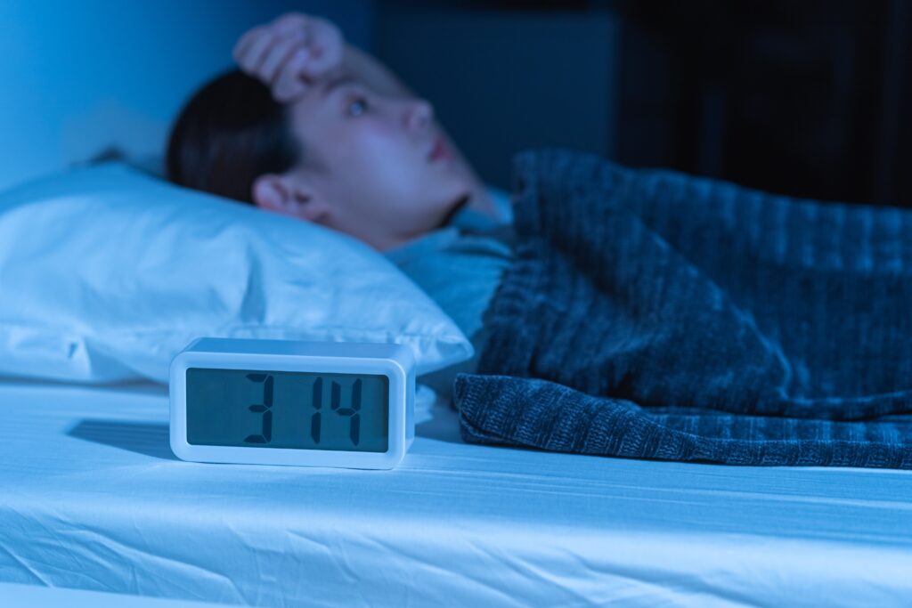 A woman laying awake in bed in front of the clock experiencing insomnia from alcohol detox.