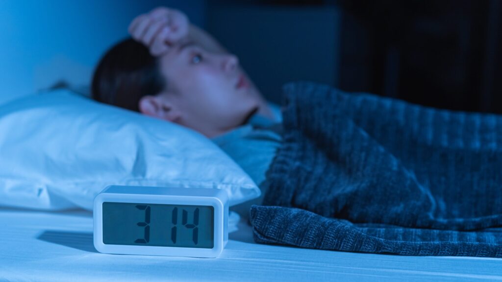 A woman laying awake in bed in front of the clock experiencing insomnia from alcohol detox.