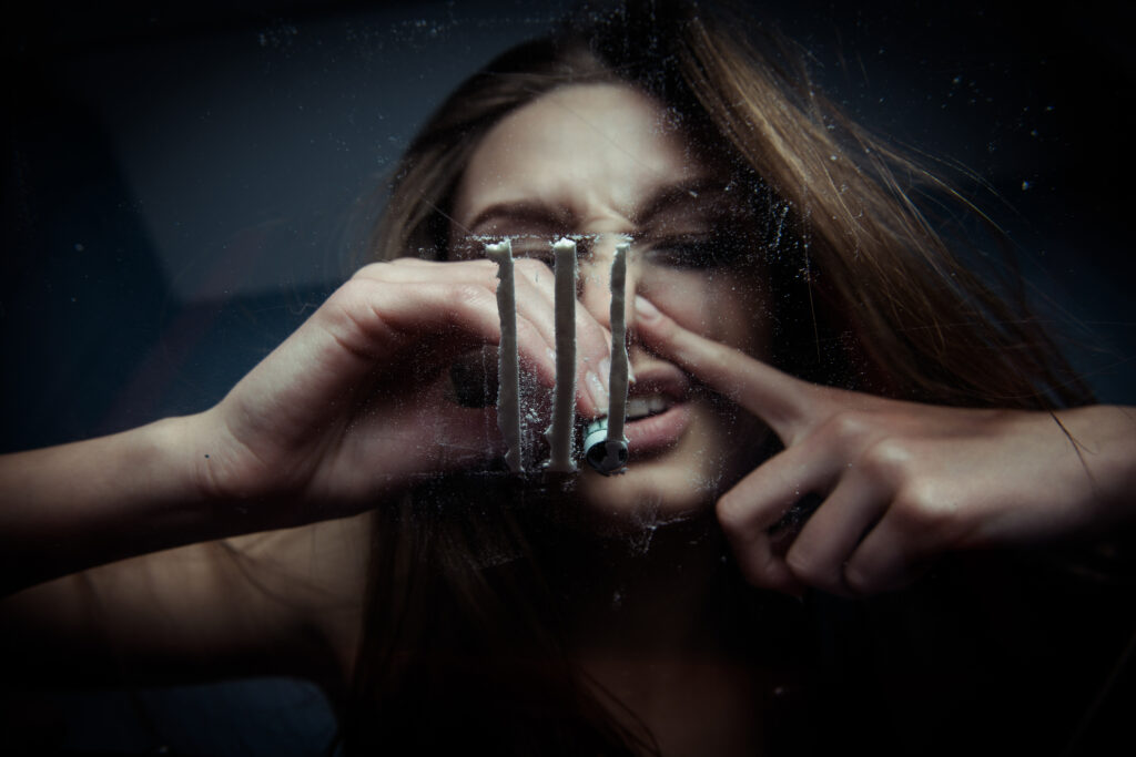 A young woman snorting lines of cocaine on a glass table and is susceptible to cocaine nose damage.