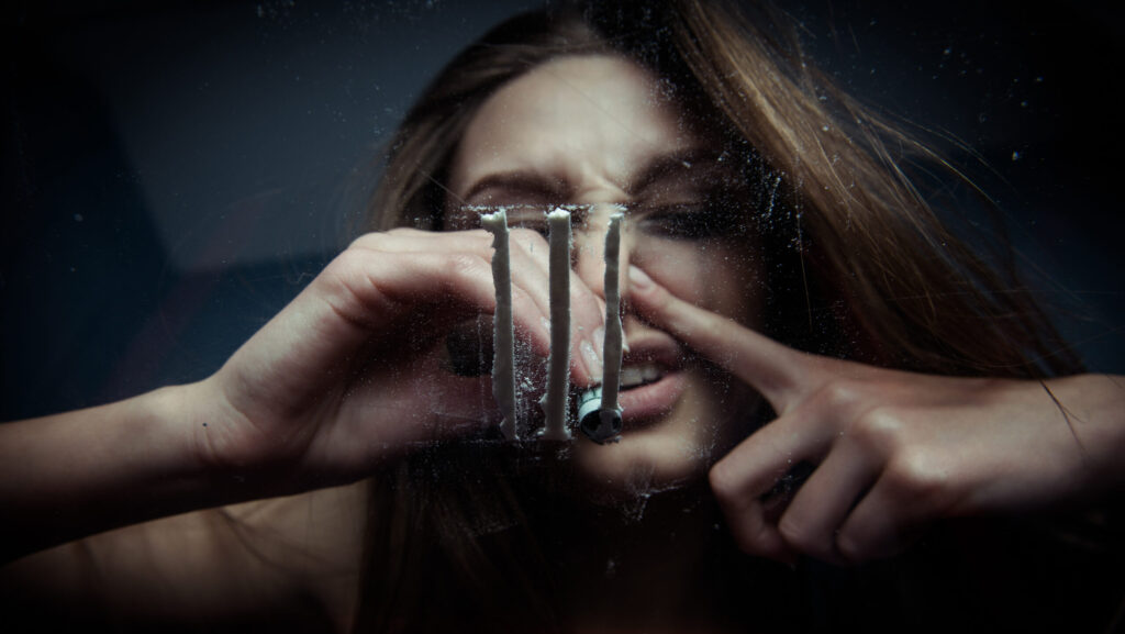 A young woman snorting lines of cocaine on a glass table and is susceptible to cocaine nose damage.