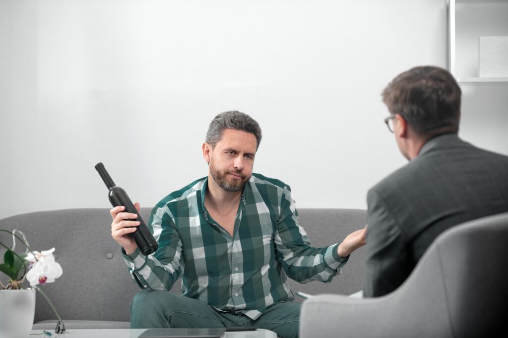 A man holding a bottle of wine is talking to a male family member as they struggle with how to live with an alcoholic.