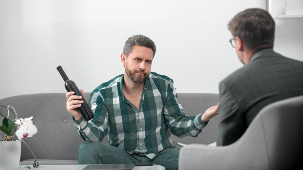 A man holding a bottle of wine is talking to a male family member as they struggle with how to live with an alcoholic.