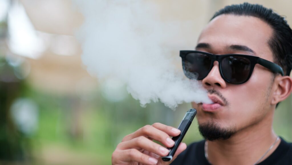 Man with sunglasses vaping and wondering is vaping bad for your teeth.