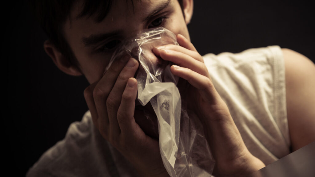 A young man with inhalant use disorder is bagging chemicals from household items with a clear plastic bag.