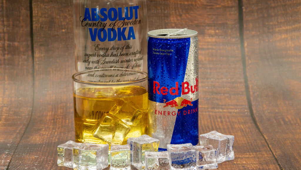 A bottle of Absolut Vokda, a can of Red Bull and a glass of the drink mixture sit on a table representing how common it is for people to mix caffeine and alcohol.